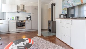 A modern kitchen with white cabinets, a stove, and a black wood-burning stove. There is a painting on the wall and a rug on the floor. - Hafenriff - Appartement 4 (Sassnitz)