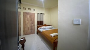 A room with a bed, a wooden door, a small table, and a light switch on the wall. - Capital O 93124 Lombok Northis Homestay (Tanjung)