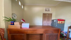 A wooden dining table with a laptop, a plant, and a flag. There is a refrigerator and a door in the background. - Capital O 93124 Lombok Northis Homestay (Tanjung)