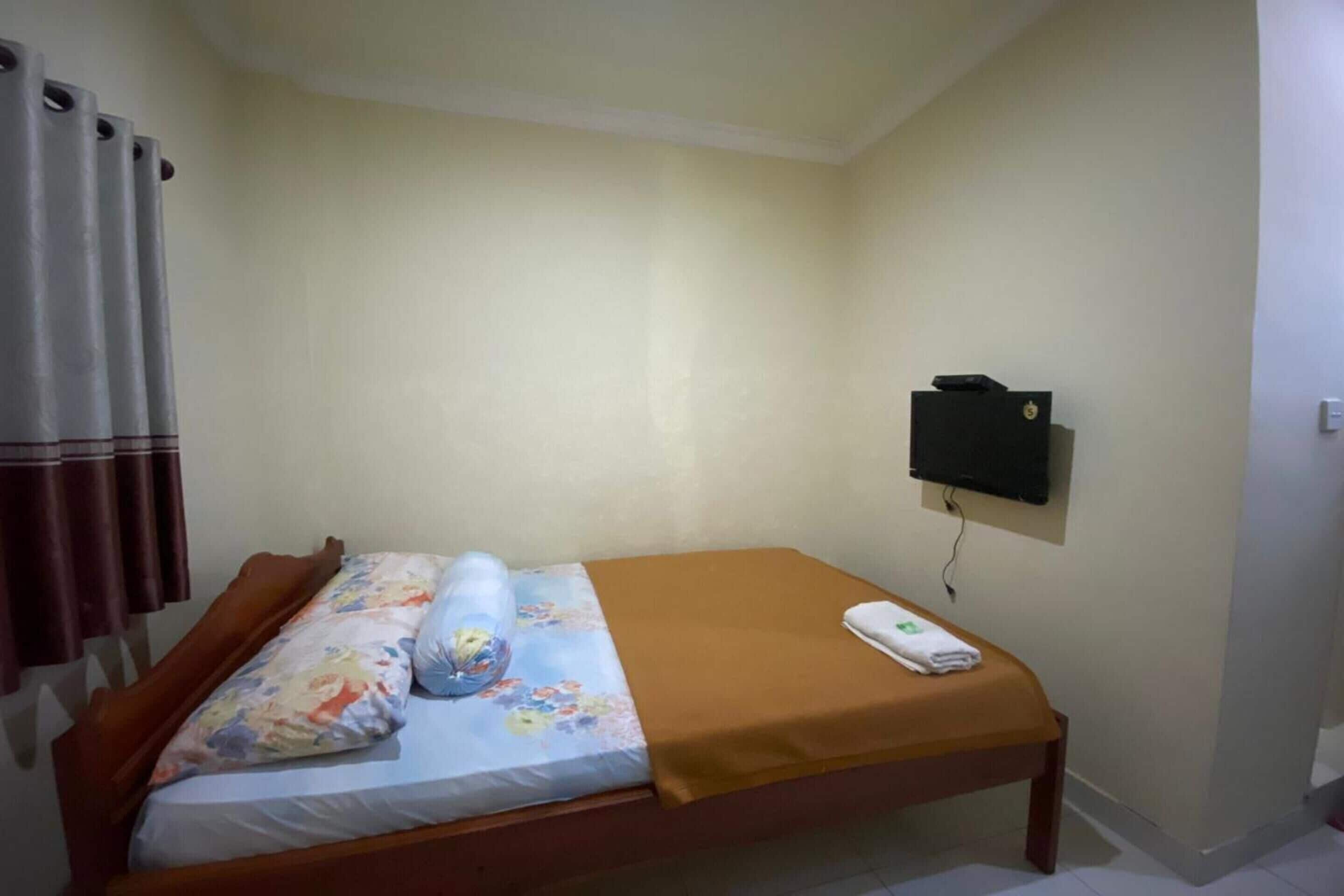 A single bed with a floral bedspread, a brown blanket, and a white pillow. There is a TV mounted on the wall to the right of the bed.
