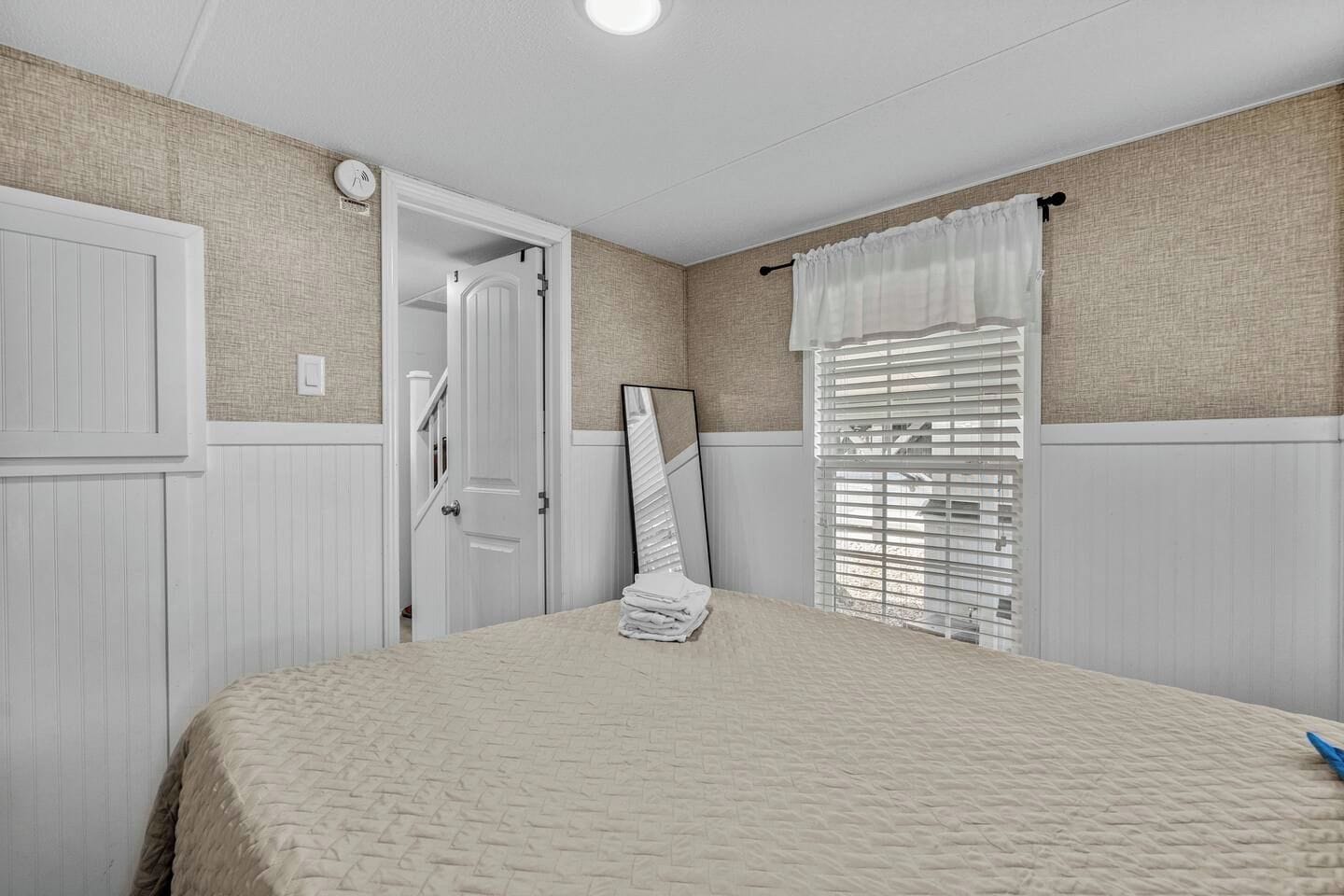 Een slaapkamer met een bed, een deur, een spiegel en een raam met jaloezieën.
