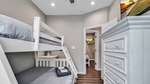Une chambre avec des lits superposés, une commode et un couloir menant à une autre pièce.