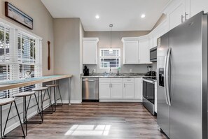 Una cocina moderna con gabinetes blancos, electrodomésticos de acero inoxidable y una barra con taburetes.