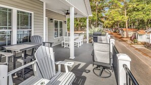 Une terrasse extérieure couverte, avec des chaises et des tables Adirondack blanches, un barbecue et une vue sur une rue résidentielle.