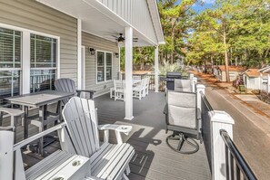 A covered outdoor patio with white Adirondack chairs and tables, a grill, and a view of a residential street. - Ocean Lakes Oasis, Golf Cart and Beach Access! (Myrtle Beach)