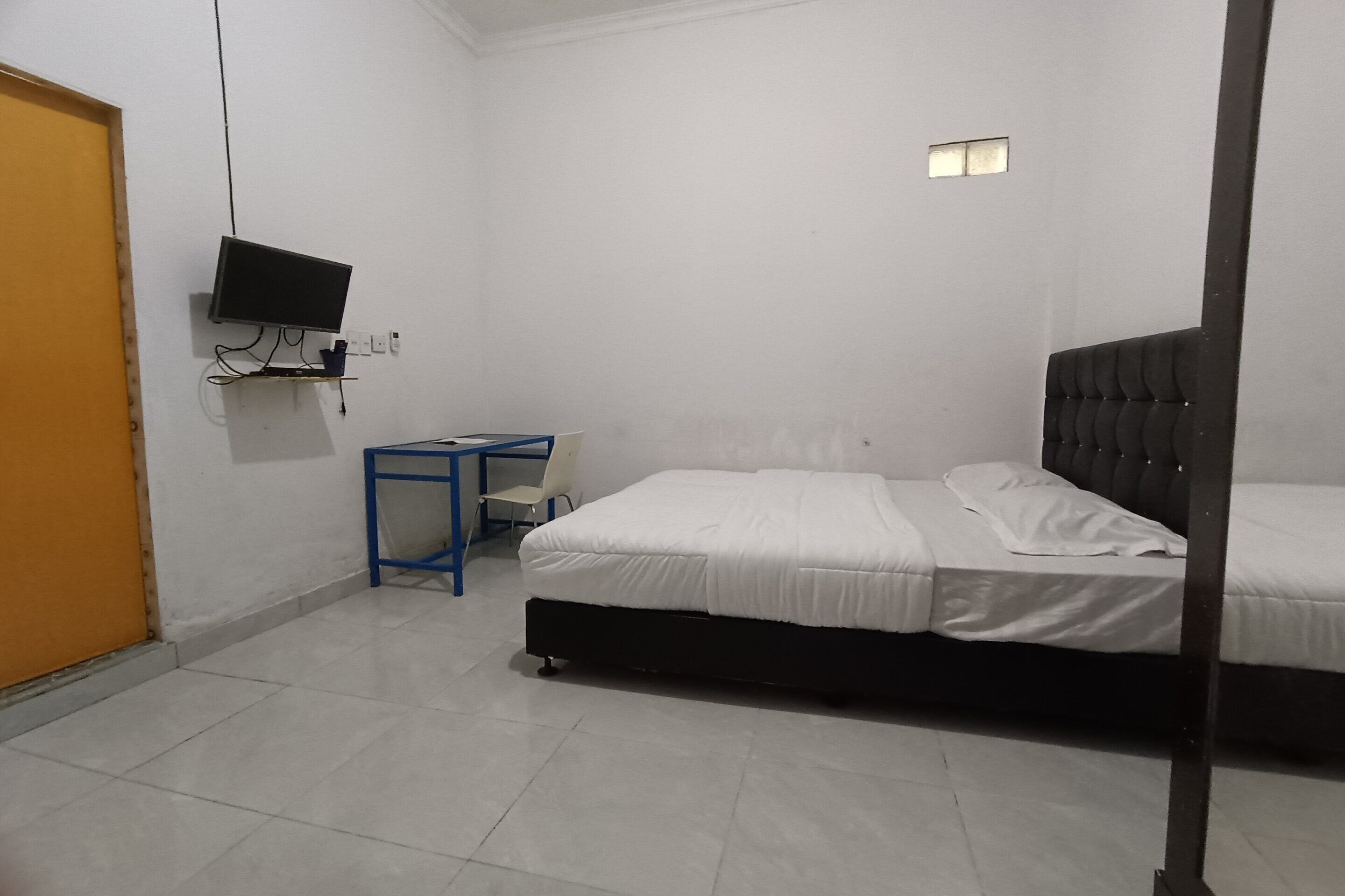 Una habitación con cama, televisor en la pared, escritorio y silla, y una puerta.