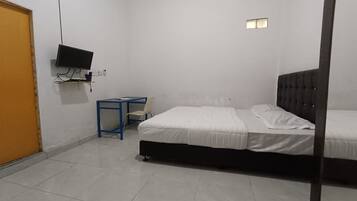 Una habitación con cama, televisor en la pared, escritorio y silla, y una puerta.