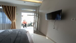 Hotellihuone, jossa on sänky, seinälle asennettu televisio ja ovi, joka johtaa parvekkeelle.
