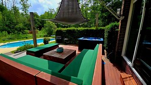 A wooden deck with green cushioned seating, a hot tub, and a pool in the background.