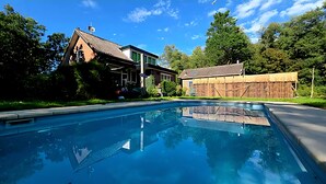 A swimming pool with a house and wooden structures in the background.