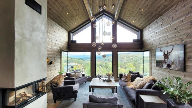 A spacious living room with a high ceiling, large windows offering a view of the outdoors, and a fireplace. - Awesome home in Norheimsund with sauna (Norheimsund)
