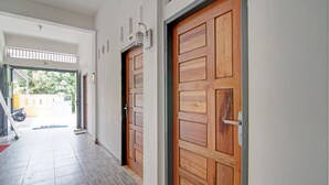 A hallway with wooden doors, a tiled floor, and a view of the outside. - Hotel O Penginapan Budhe Sri (Koealabadak)