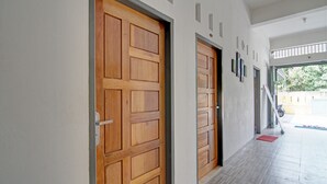 A hallway with two wooden doors, a tiled floor, and a view of the outside. - Hotel O Penginapan Budhe Sri (Koealabadak)