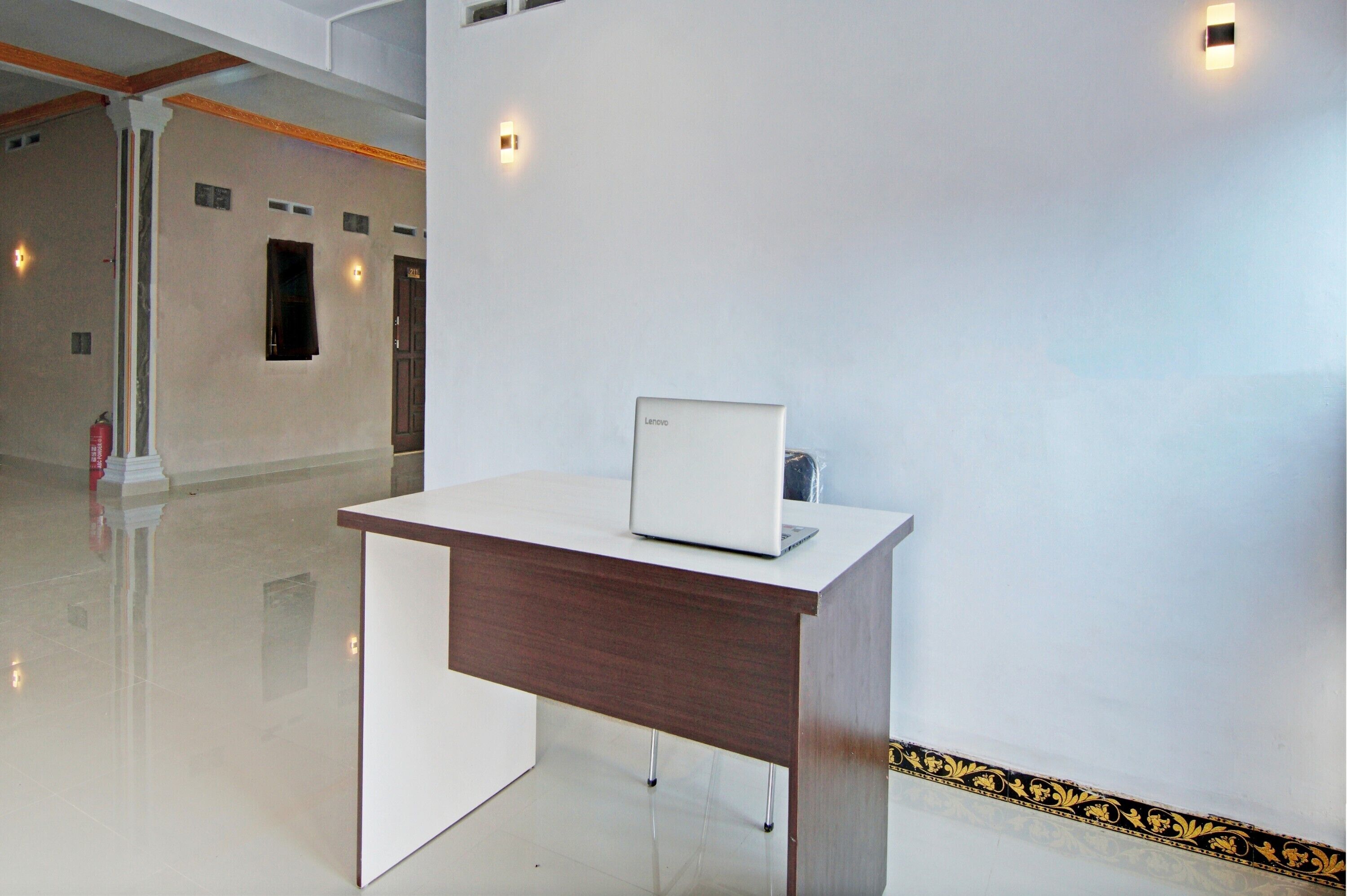 A modern office space with a white desk and a laptop, a fire extinguisher, and a decorative border on the wall.
