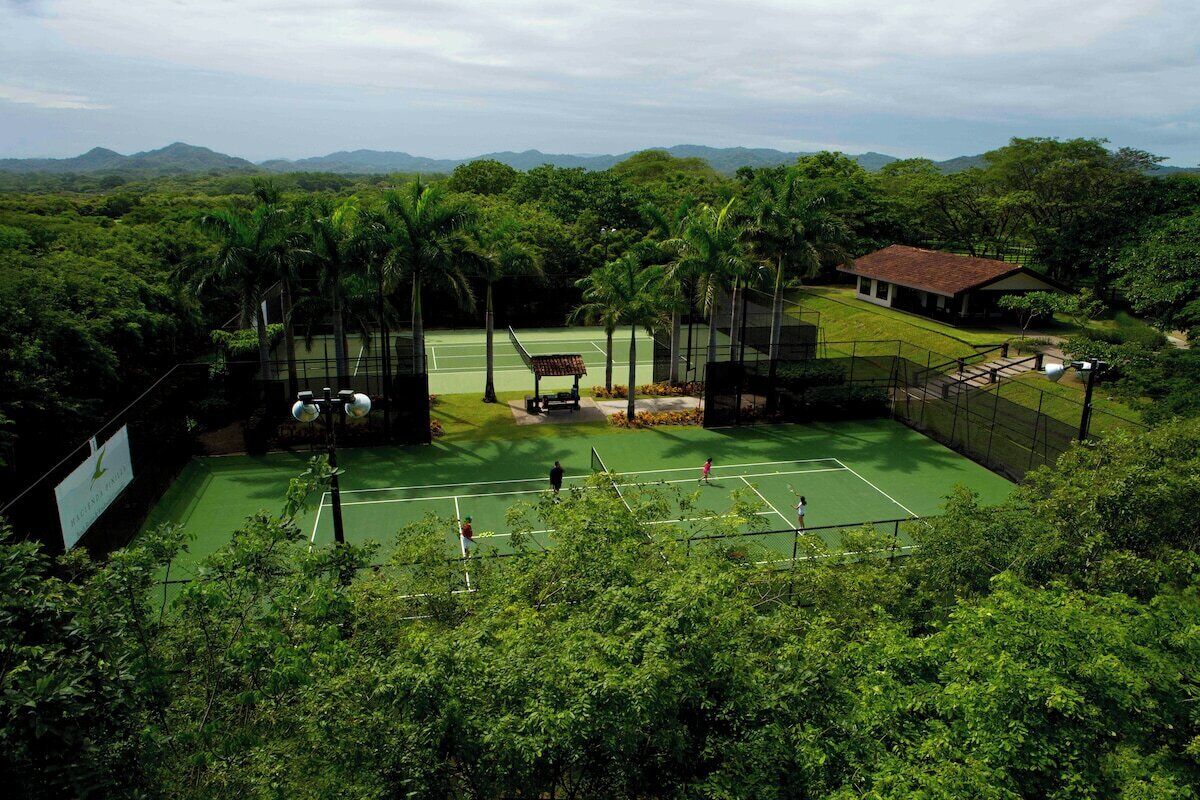 A tennis court surrounded by lush greenery and a mountain backdrop.