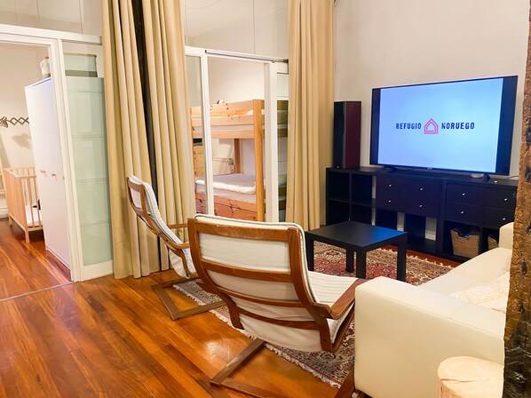 Une pièce chaleureuse avec un lit superposé en bois, une télévision, un canapé blanc et une chaise en bois.