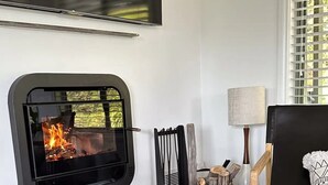 Una sala de estar con chimenea, un televisor montado encima y un rincón de estar cómodo con un sillón y un sofá.