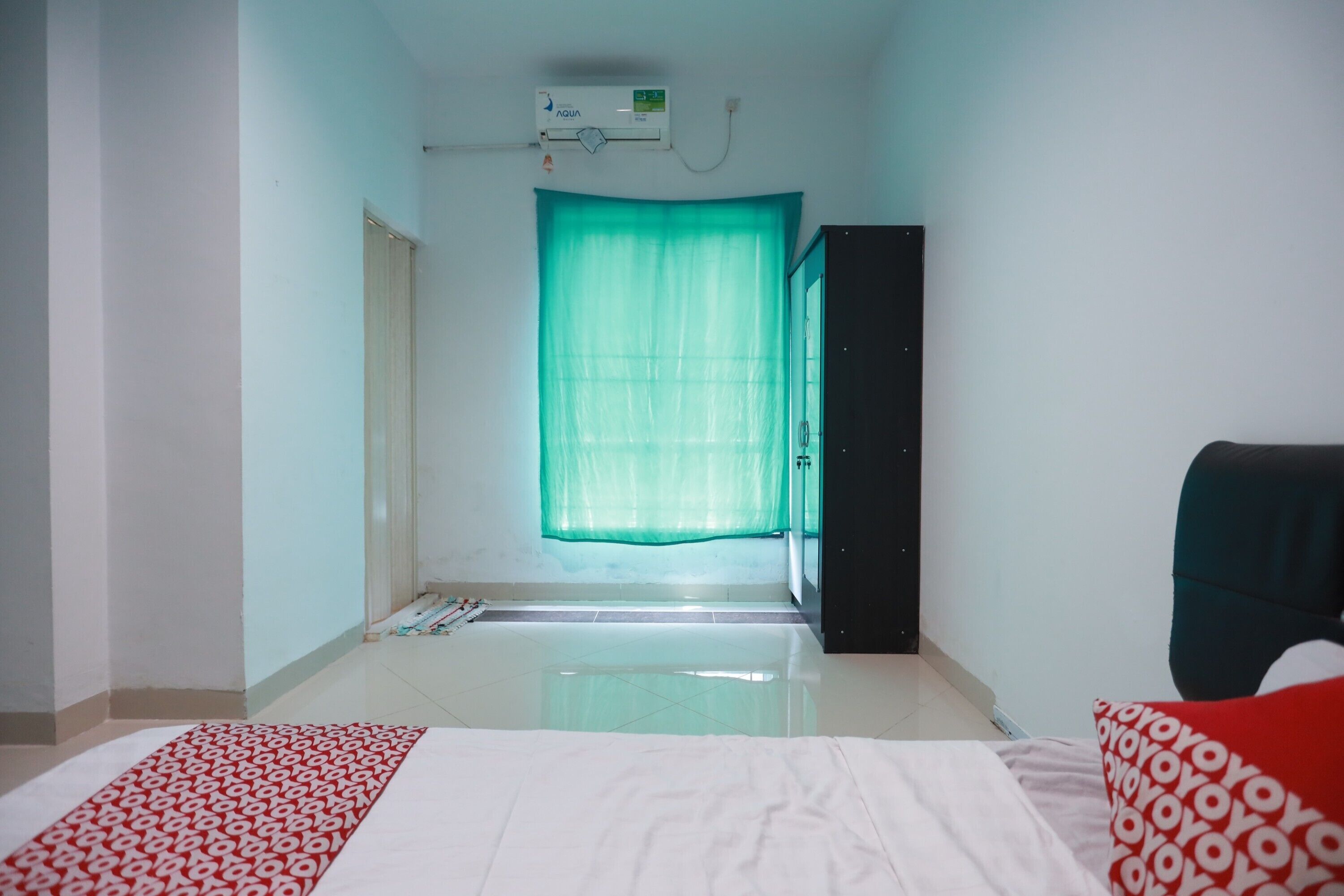 A hotel room with a bed, a wardrobe, a window with a green curtain, and a ceiling air conditioner.