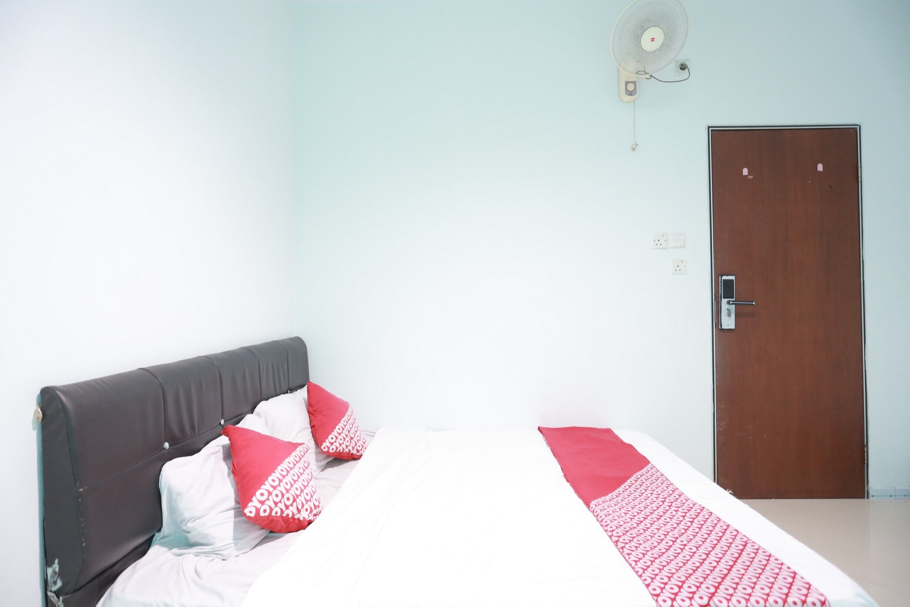 A bedroom with a bed, a wooden door, and a wall-mounted fan.