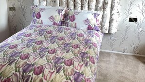 Ein Schlafzimmer mit blumigem Bettbezug, einem Holzkopfteil und einem Teppichboden.