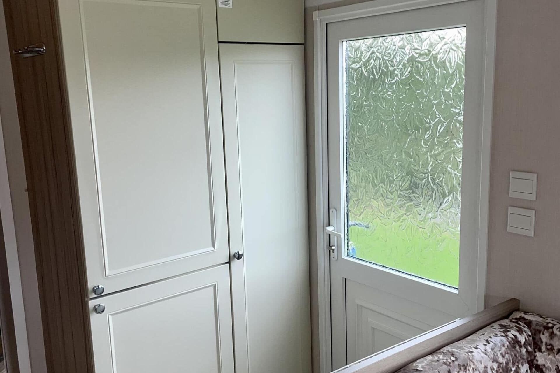 Une pièce avec une porte blanche, une fenêtre à vitres dépolies et une vue sur la verdure à l’extérieur.