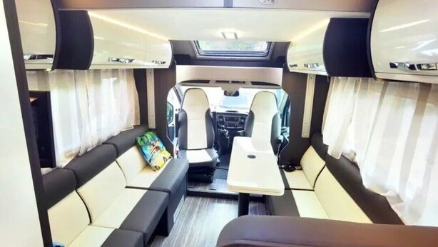 Interior compacto de una autocaravana, con zona de estar central, una mesita y cortinas laterales.