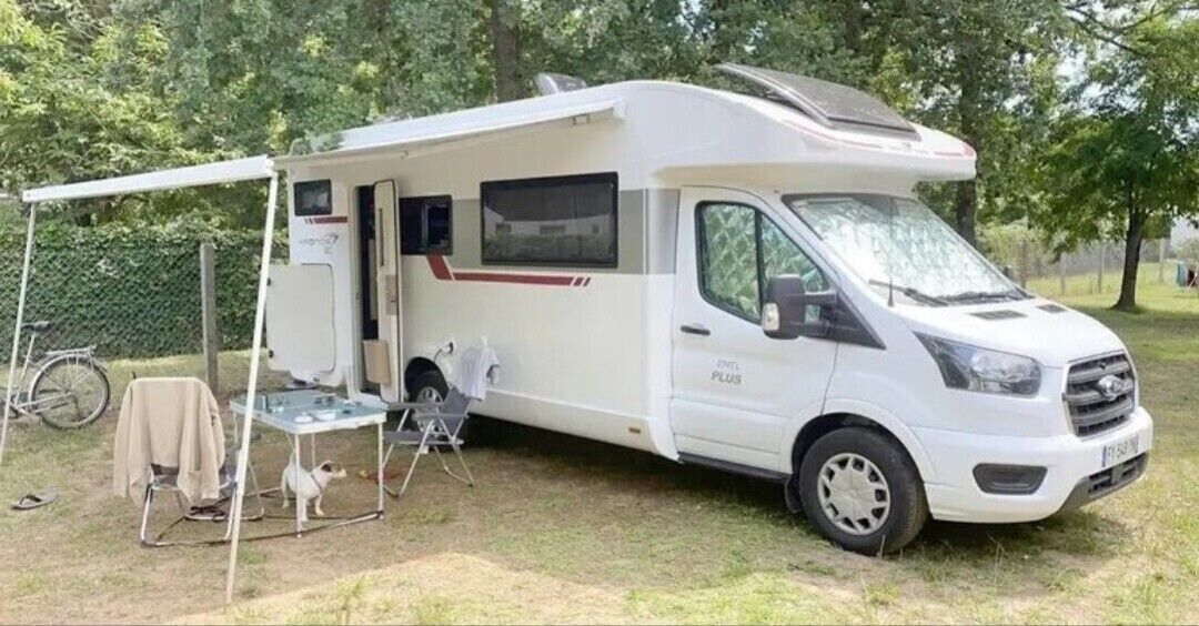 A white RV with a covered living area, a table, and a small dog.