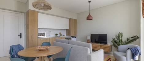 Una sala de estar moderna con un sofá gris, sillas azules, una mesa de comedor de madera y una cocina al fondo.