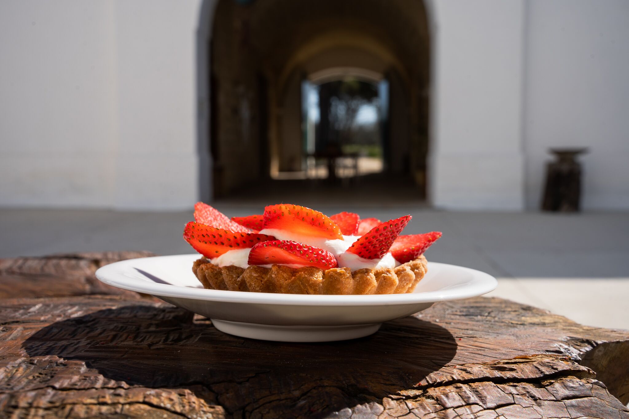 Un postre en un plato blanco con fresas y crema batida, sobre una mesa de madera de aspecto rústico.