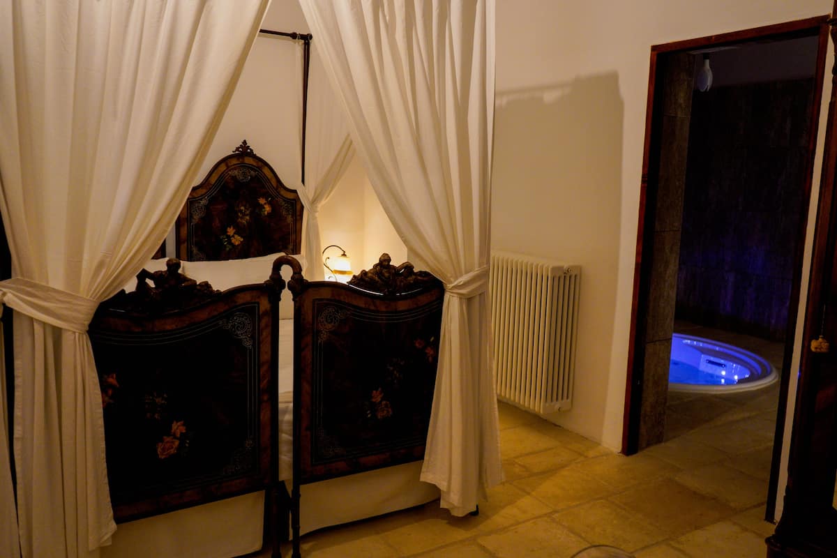 A bedroom with a four-poster bed, a nightstand, and a bedside table with a lamp.