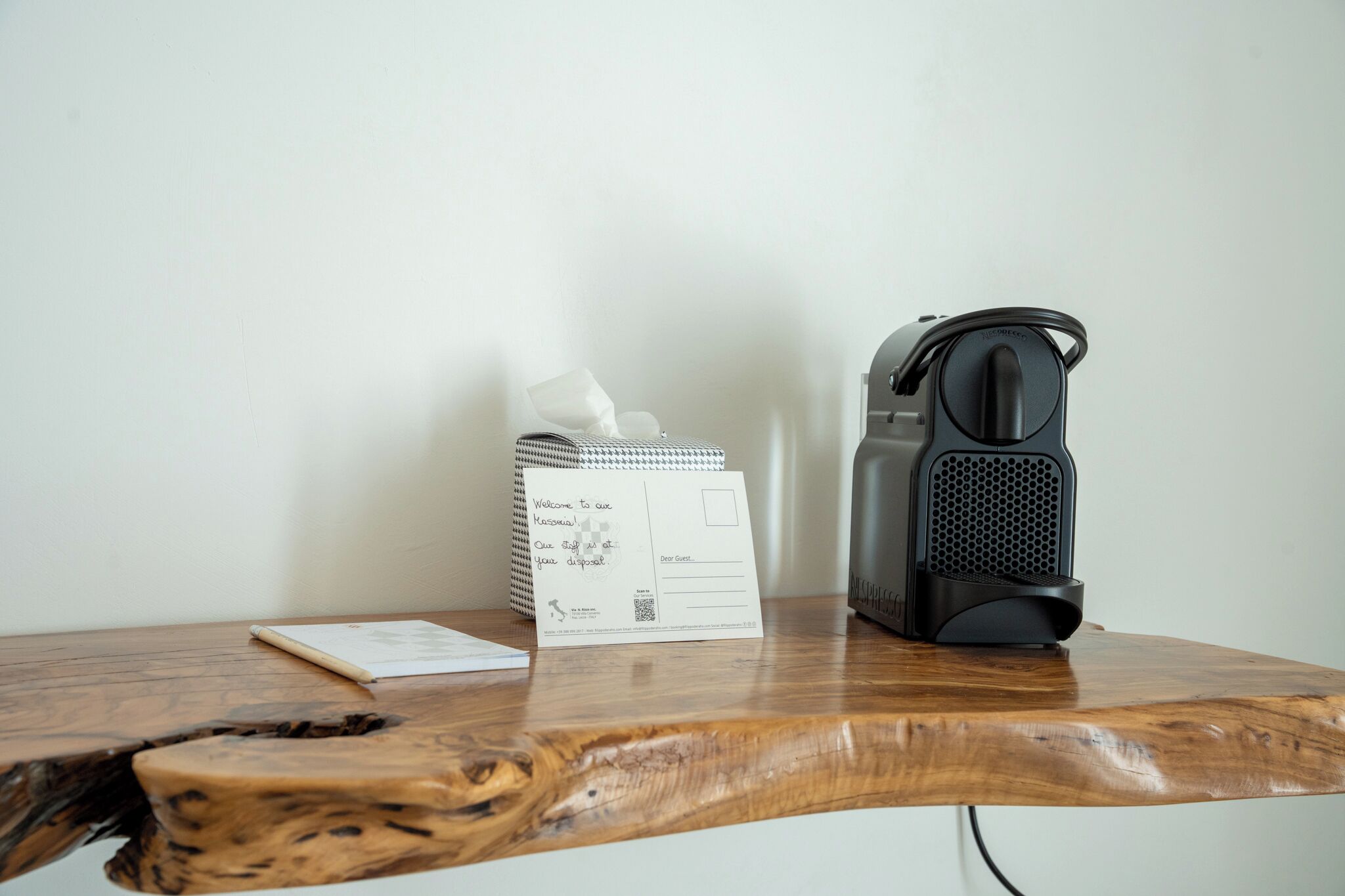 Una mesa de madera con una caja de pañuelos, un bloc de notas y una máquina de café espresso negra.