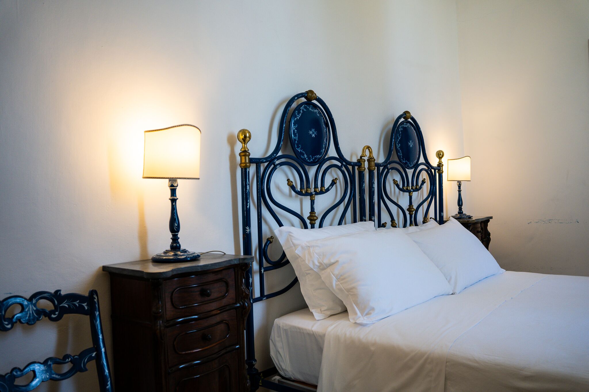 Un dormitorio con cama, dos mesitas de noche con lámparas, un aparador y una silla.