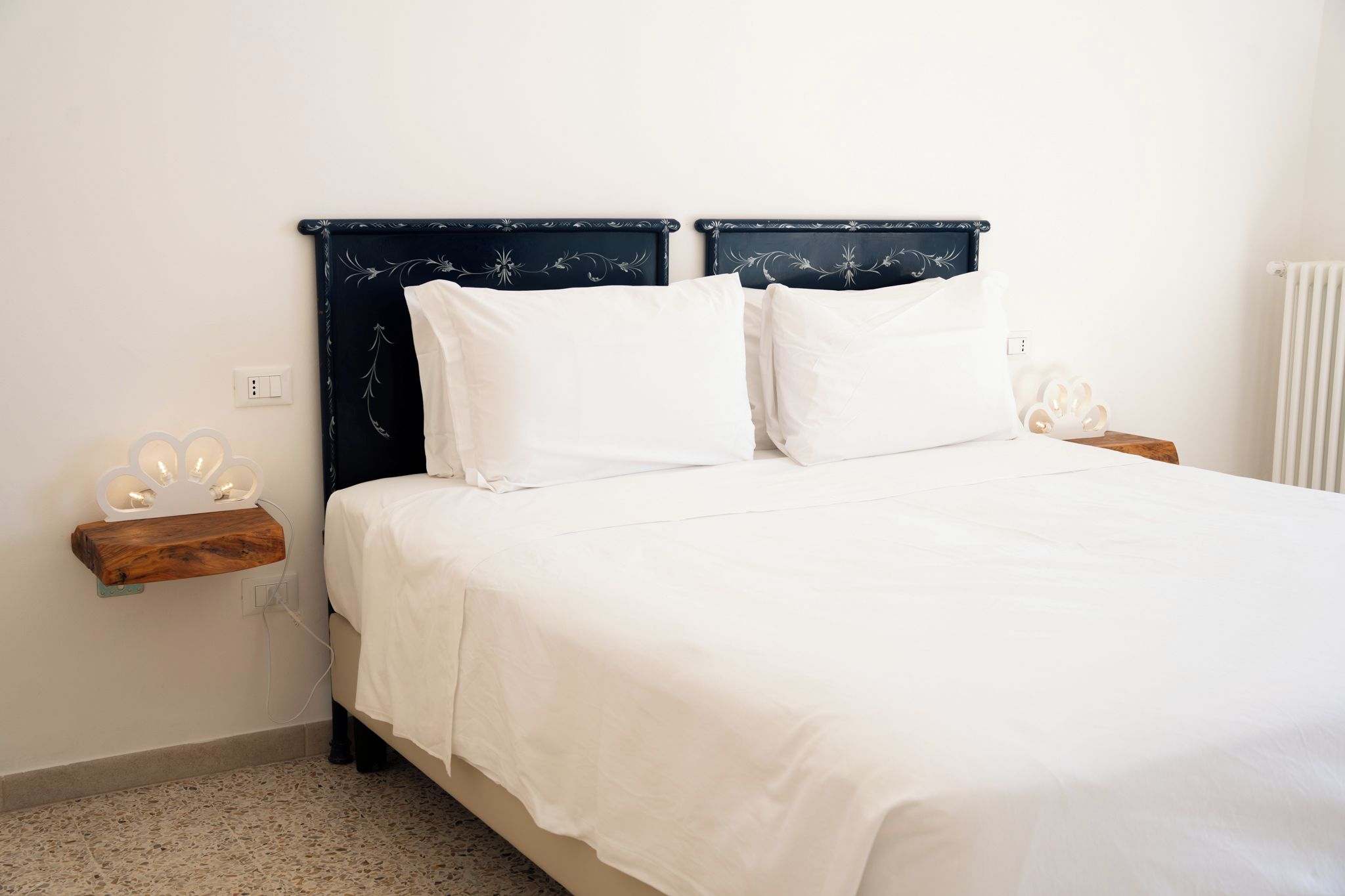 Una cama con cabecera oscura, ropa de cama blanca y una mesita de noche con lámpara.