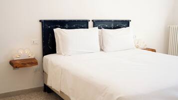 Una cama con cabecera oscura, ropa de cama blanca y una mesita de noche con lámpara.