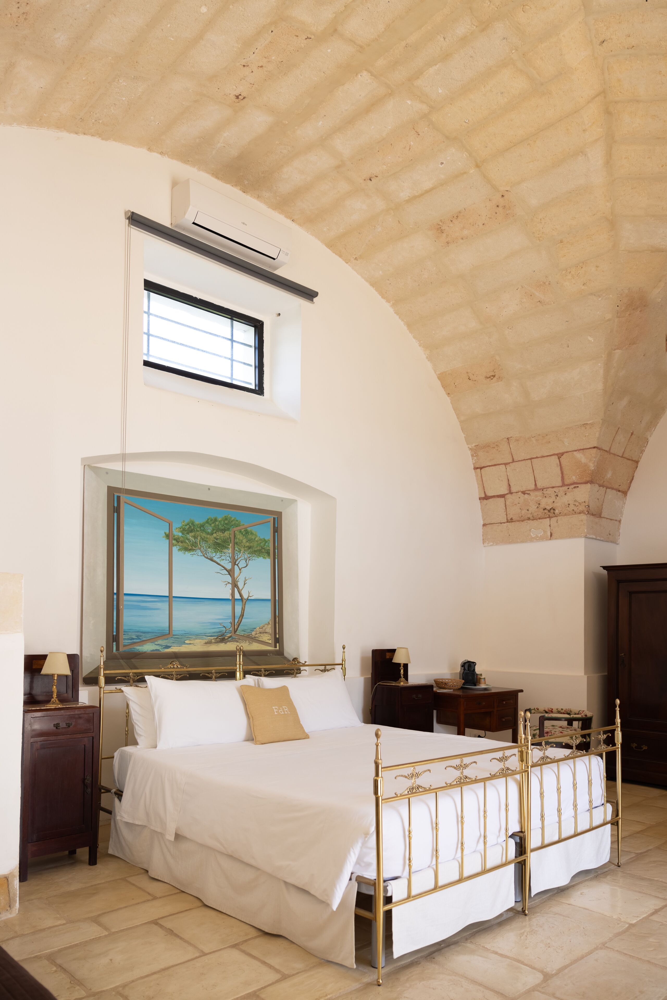 A bedroom with a large bed, a painting of a tree and sea, a window, and a wooden ceiling.