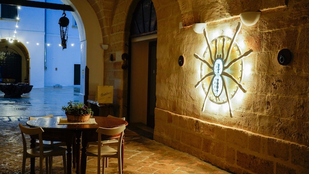 A stone-walled courtyard with a table and chairs, a hanging light fixture, and a wall-mounted decorative piece.
