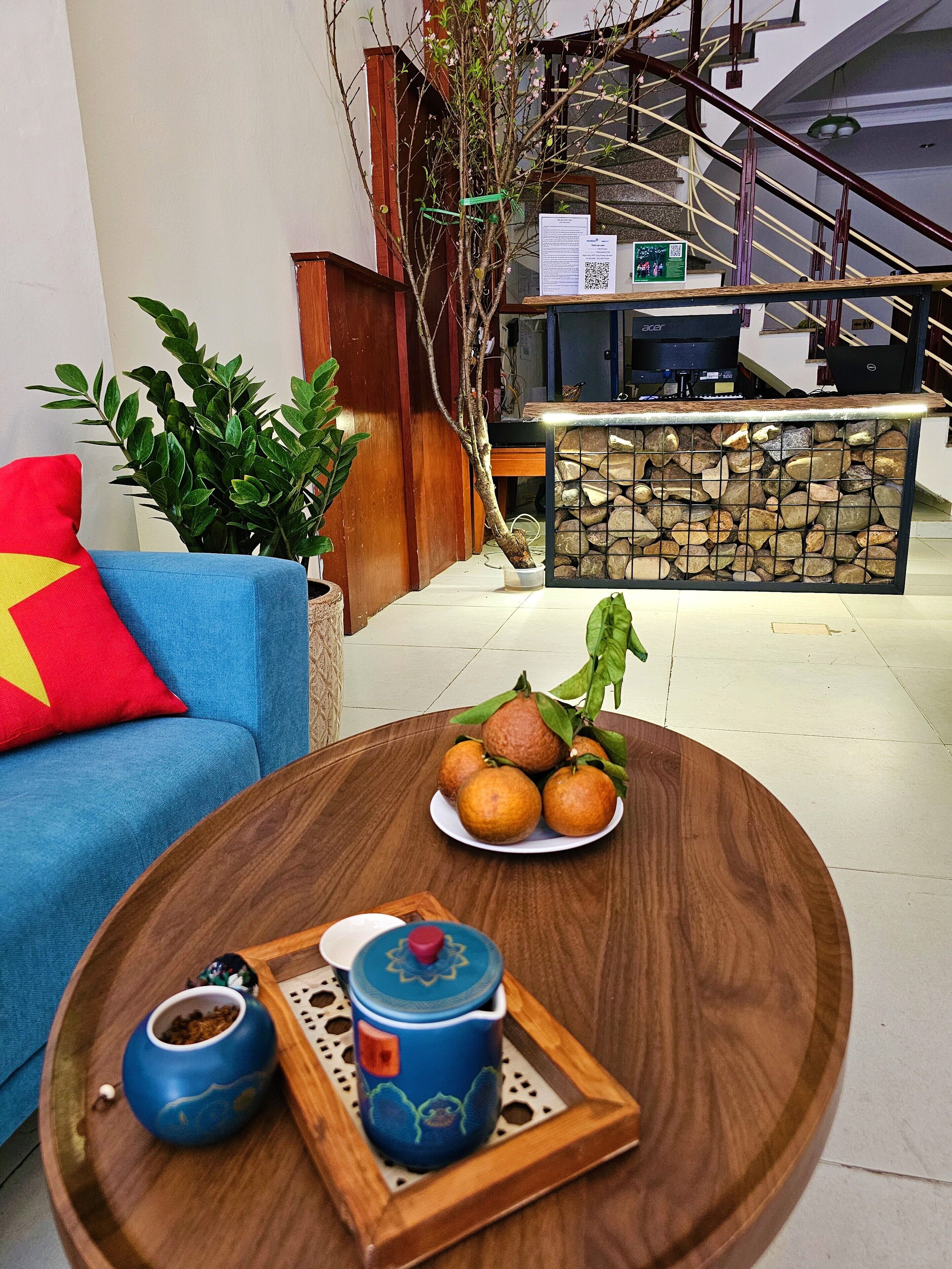 Ein Zimmer mit einem blauen Sofa, einem Holztisch mit Teekanne und Orangen sowie einer Treppe im Hintergrund.