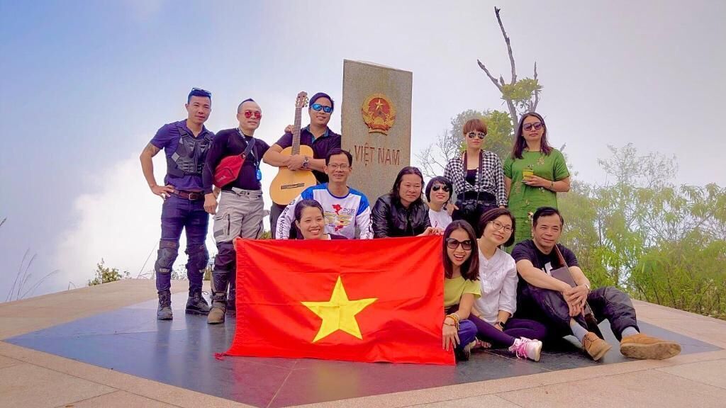 Un groupe de personnes posant devant un drapeau et un monument, dans un cadre extérieur.