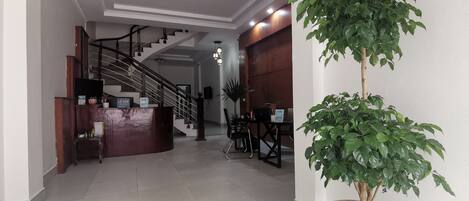 A hotel lobby with a reception desk, a staircase, and a potted plant.