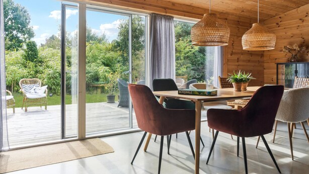 Ein moderner Essbereich mit einem Holztisch, vier Stühlen und Blick auf einen üppigen Garten durch große Schiebeglasfenster.