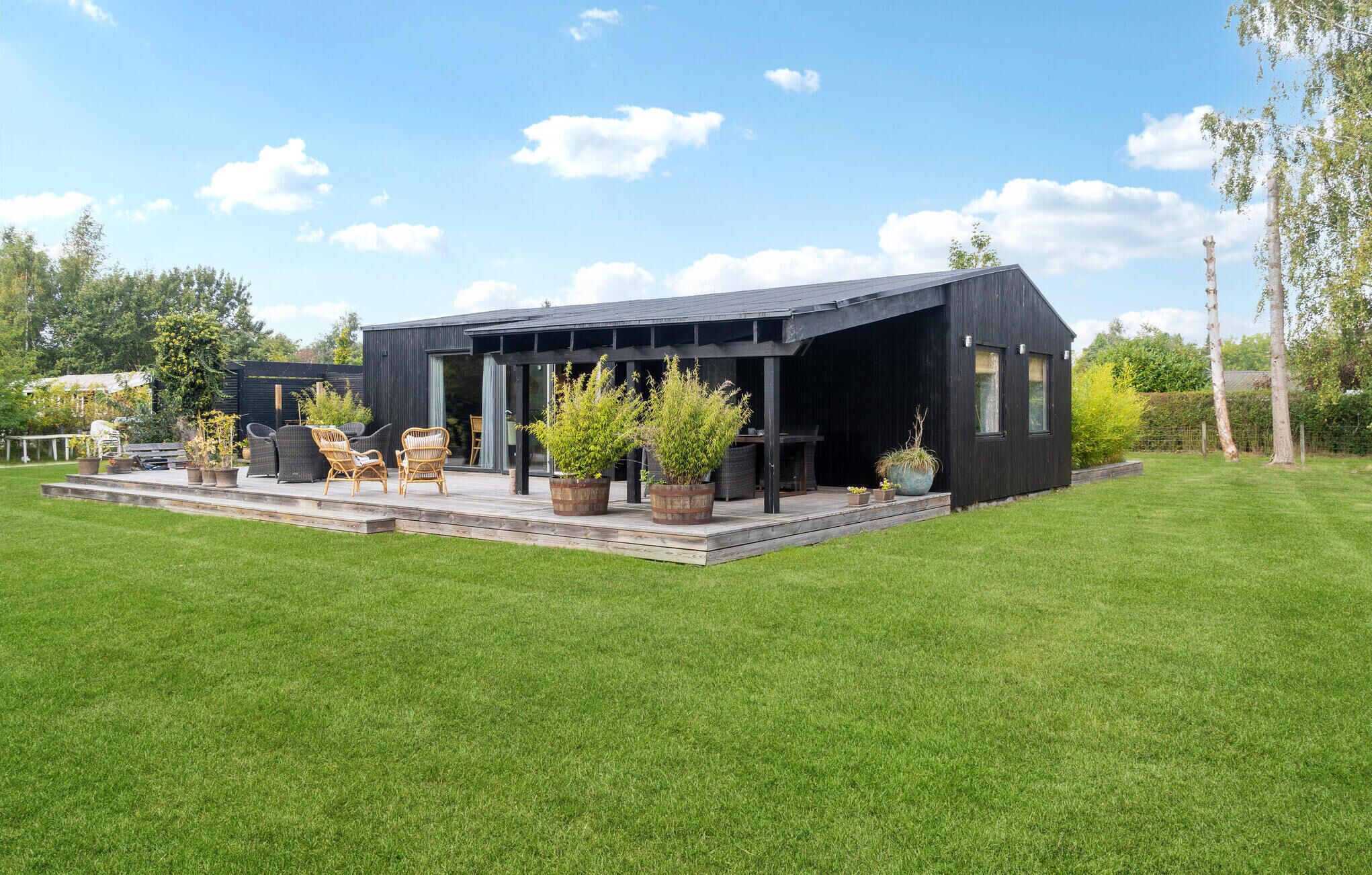 Un bâtiment moderne de couleur noire, doté d’un patio couvert, entouré d’une pelouse bien entretenue et d’arbres.