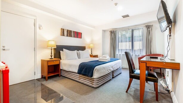 Habitación de hotel con cama, mesitas de noche, escritorio, silla, televisión y ventana con cortinas.