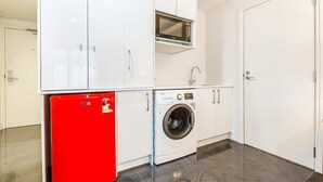 Un área de lavandería compacta con lavadora, un mini refrigerador rojo y un microondas.