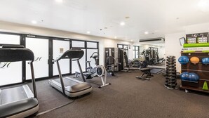 Un gimnasio con cintas de correr, elípticas, bancos de pesas y una barra de mancuernas.
