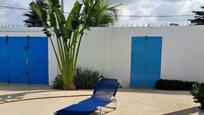 A poolside area with a blue lounge chair, a blue tiled wall, and a large plant. - Villa Neuve, Aérée et Confortable (Nianing)