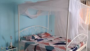 A bed with a white canopy, a bedside table with a bottle and a phone, and a wall with a blue accent. - Villa Neuve, Aérée et Confortable (Nianing)