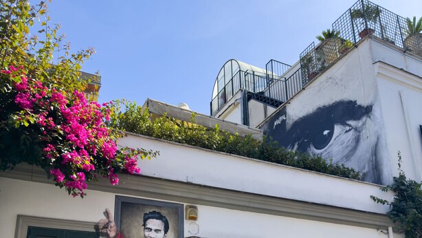 A building with a mural of a man's face, a red door, and green shutters. - Lovely Apartment in Hip and Vibrant Pigneto (Roma)