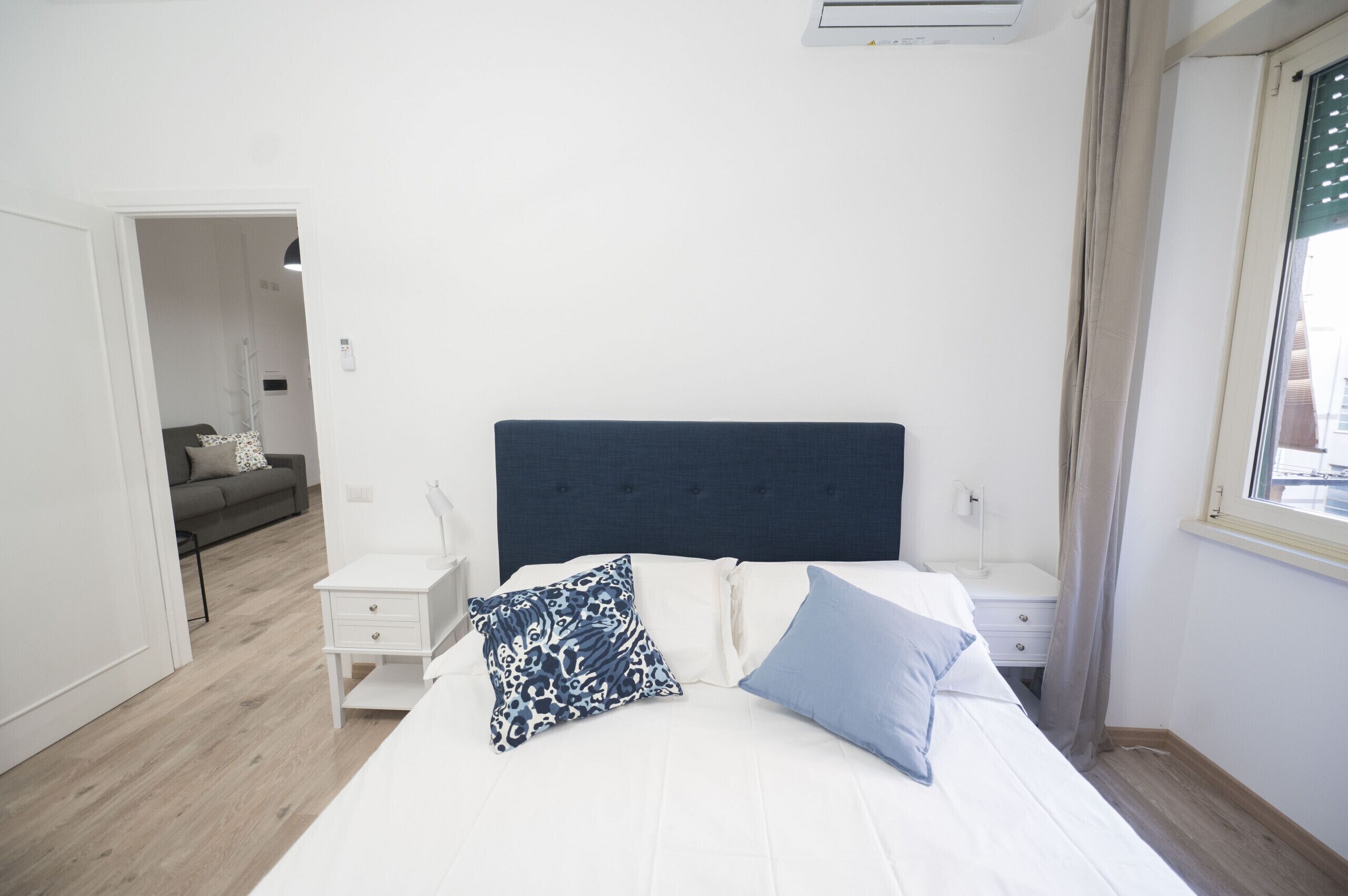 Een slaapkamer met een bed, nachtkastje, kledingkast en een raam met gordijnen.