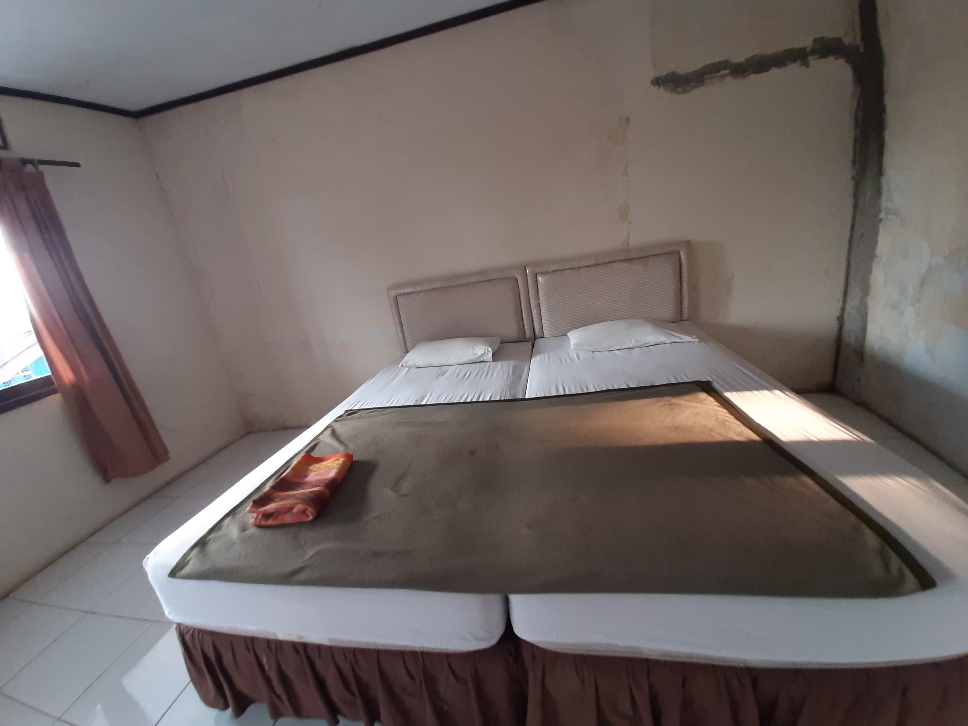 A single bed with a headboard, a window with curtains, and a tiled floor.