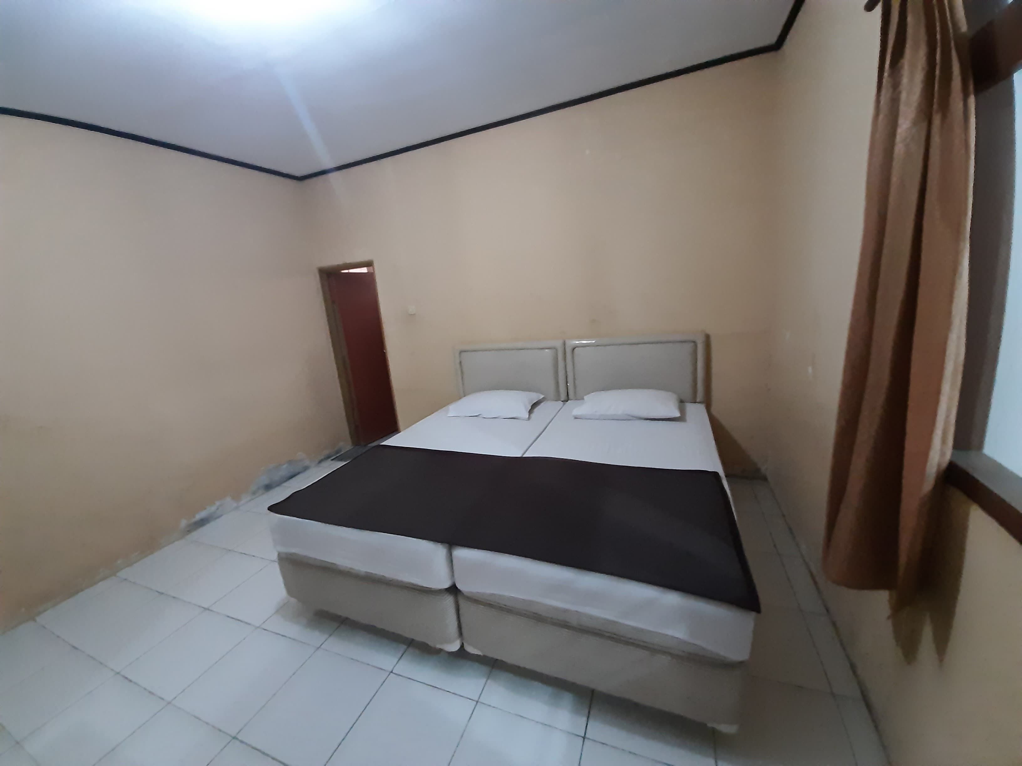 Een kleine, eenvoudige kamer met een bed, een deur en een raam met gordijnen.